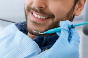 Closeup of male patient smile and dentist hands with tools