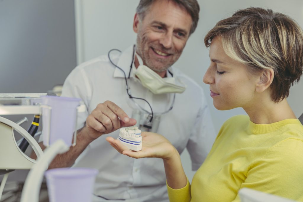 Dentist explaining dental bridg on a tooth model to his patient