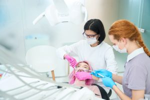 Woman orthodontist performing dental procedure to young female patient